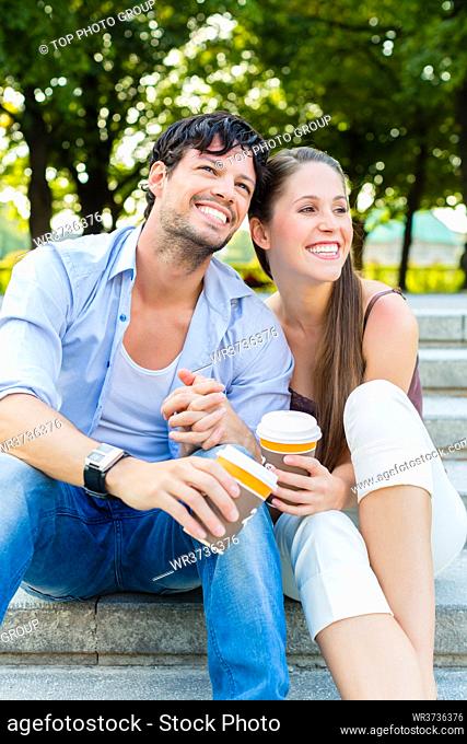 Man and woman or young couple drinking coffee and sitting in city park in summer on stairs