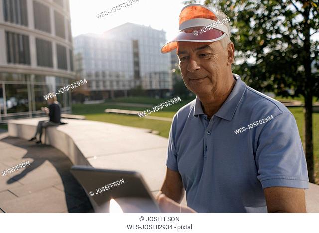 Germany, Hamburg, Hafencity, senior tourist wearing sun visor using tablet in the city