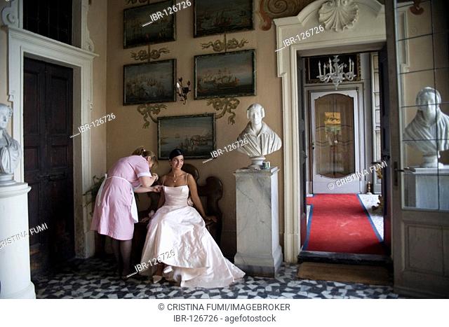 Beautiful bride having her dress arranged by a maid, Villa Sommi-Picenardi, Olgiate Molgora, Lecco, Italien