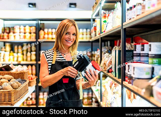 Smiling female shop attendant labeling jar at store