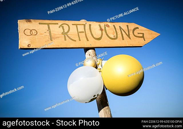 12 June 2022, Baden-Wuerttemberg, Rottweil: A wooden sign with balloons attached to it points the way to a free wedding ceremony at the edge of a dirt road