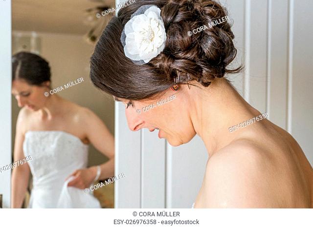 A beautiful bride dresses herself in front of the mirror
