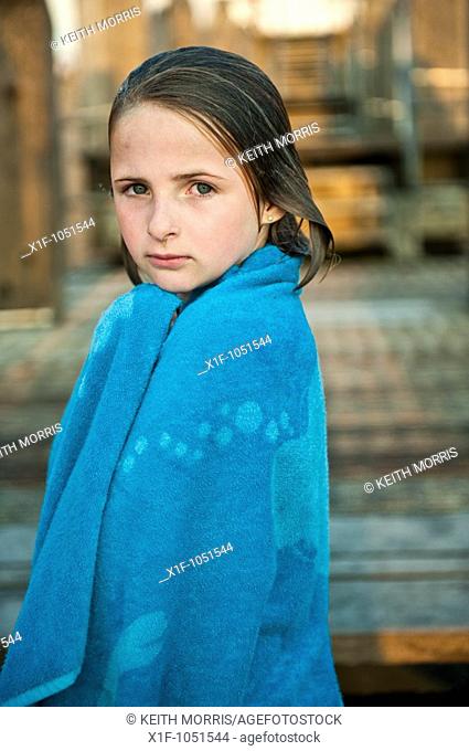 Ten year old girl wrapped in a blue towel after swimming in the sea, wet hair, looking at the camera