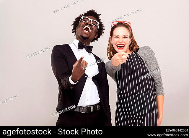 Ridicule, taunt concept. Two friends pointing fingers at camera and smiling. Studio shot, gray background