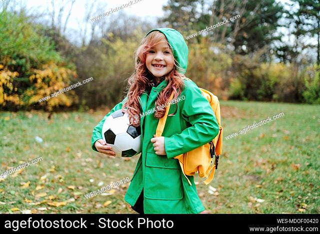 Happy girl standing with backpack and soccer ball at park