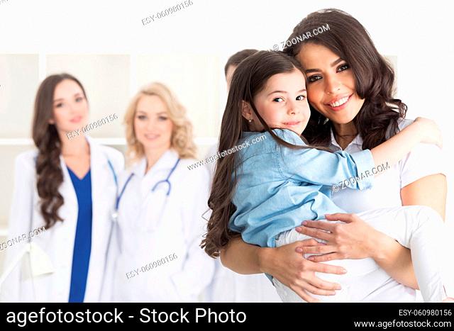 Mother and daughter in medical clinic, team of doctors on background