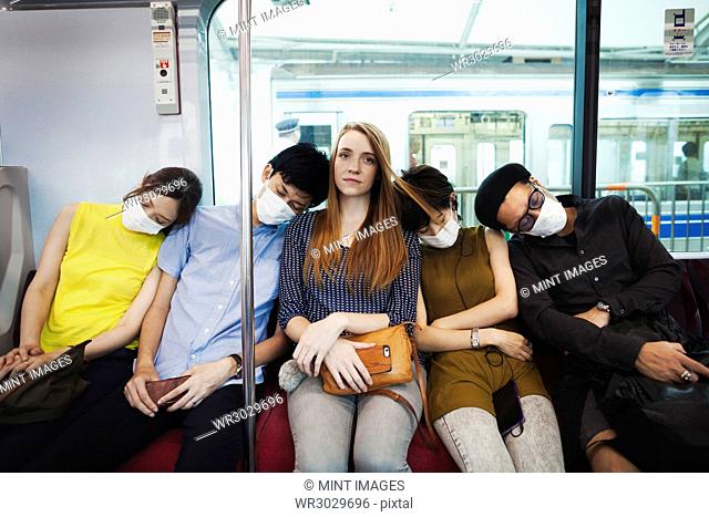 Five people wearing dust masks sitting sidy by side on a subway train, Tokyo commuters