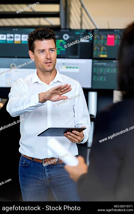 Mature businessman holding tablet PC discussing with businesswoman in industry