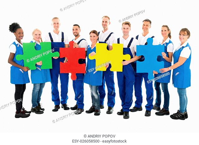 Portrait of confident janitors holding jigsaw pieces while standing in row against white background