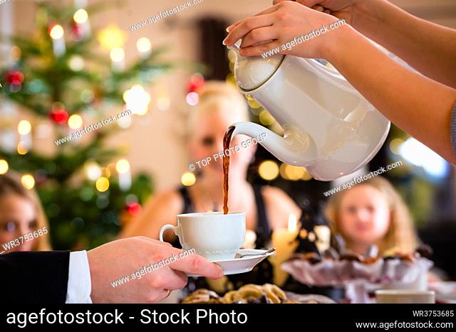 Family celebrating Christmas with drinking coffee and X-mas cookies, mom filling a cup