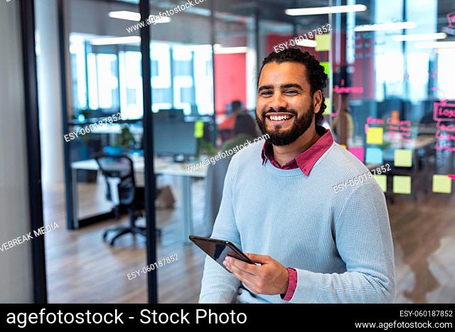 Portrait of mixed race male creative worker using tablet computer and smiling