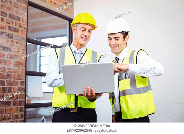 Smiling architects discussing while holding blueprint