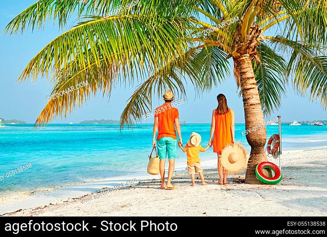 Family on beach, young couple in orange with three year old boy under the palm tree. Summer vacation at Maldives