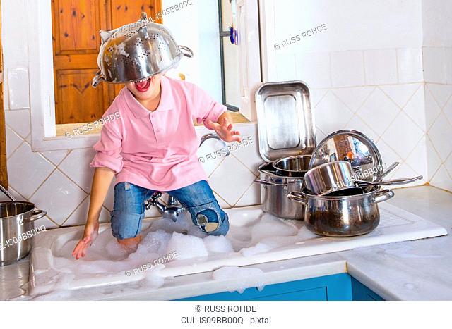 Boy playing in kitchen sink with colander on his head