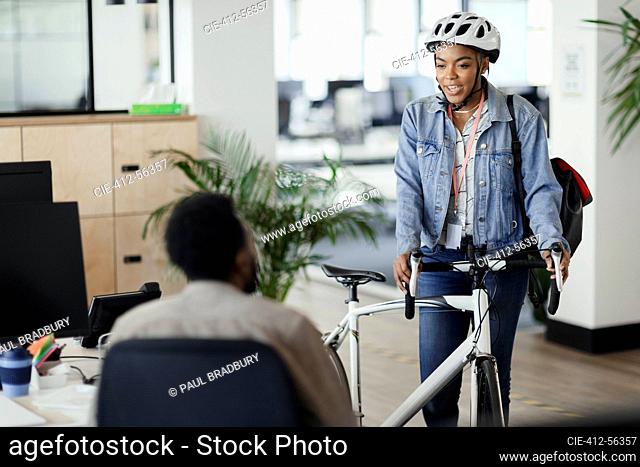 Businesswoman in helmet with bicycle talking to coworker in office