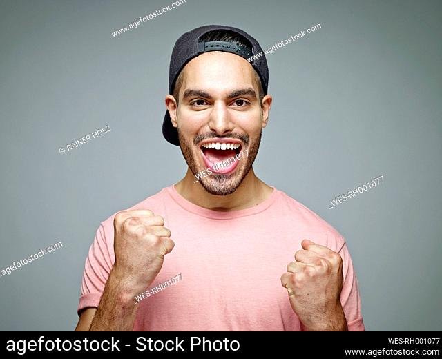 Portrait of man with baseball cap screaming for joy in front of grey background