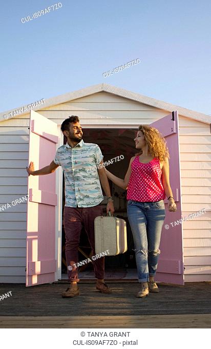 Young couple leaving beach hut with suitcase