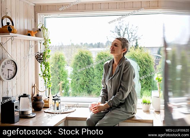 Mature woman sitting on kitchen counter at home