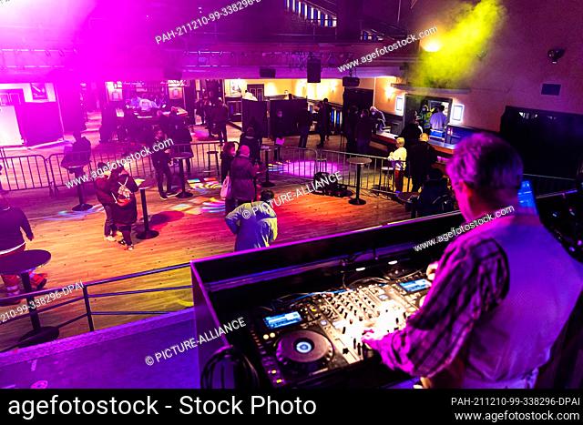 10 December 2021, Lower Saxony, Hanover: A DJ plays music on stage and in front of it people wait at bar tables for their vaccination