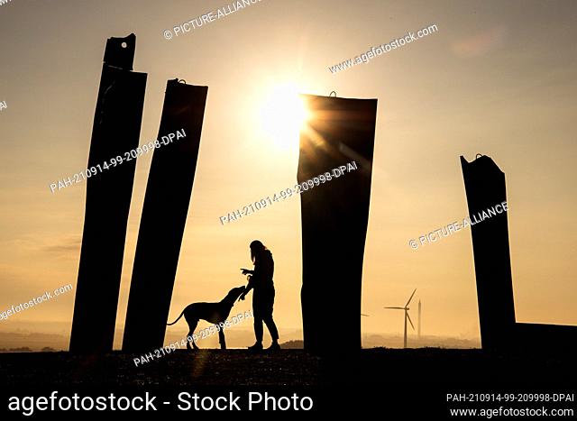 14 September 2021, Bremen: A woman walks her dog across the Metalhenge viewpoint at the Blockland Landfill at sunrise. Photo: Sina Schuldt/dpa