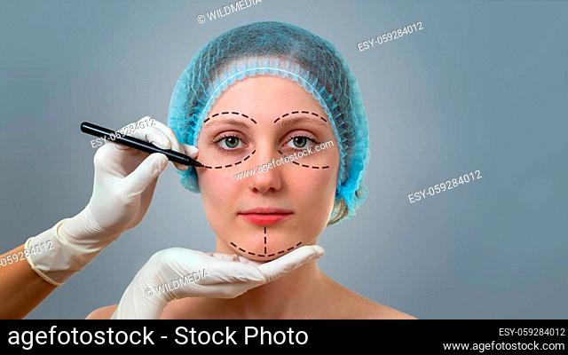 Front view of a plastic surgeon drawing lines on a face of young woman prior to cosmetic surgery. Concept of visage improvement and beauty healthcare in clinic