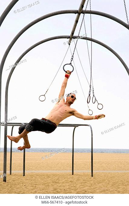 Caucasian man on the rings set, swinging from one ring to the next. Santa Monica Beach, Los Angeles, California