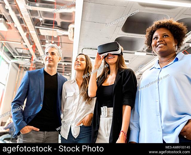 Happy businesswoman wearing VR goggles standing with colleagues in office