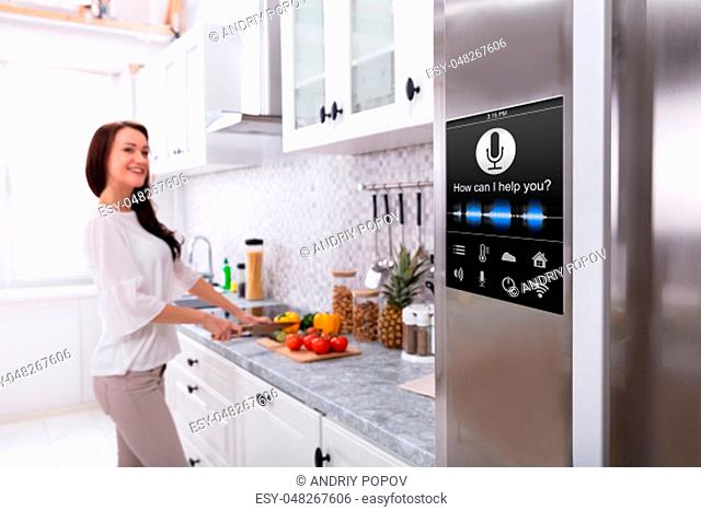 An Oven With Voice Recognition Function Near Smiling Young Woman Cutting Vegetables In Kitchen