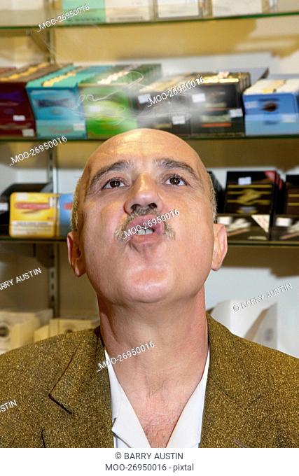 Mature man in tobacco store blowing smoke