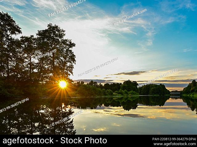 07 August 2022, Brandenburg, Berkenbrück: The late evening sun shines through the wooded bank on the Fürstenwalder Spree