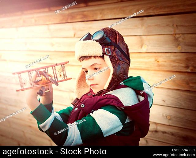 Boy playing in aviator hat with old plane at countryside