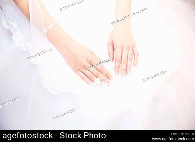 Hands bride with a manicure, on the finger of the bride wedding ring, hands on the background of white lace dress covered with a veil in studio