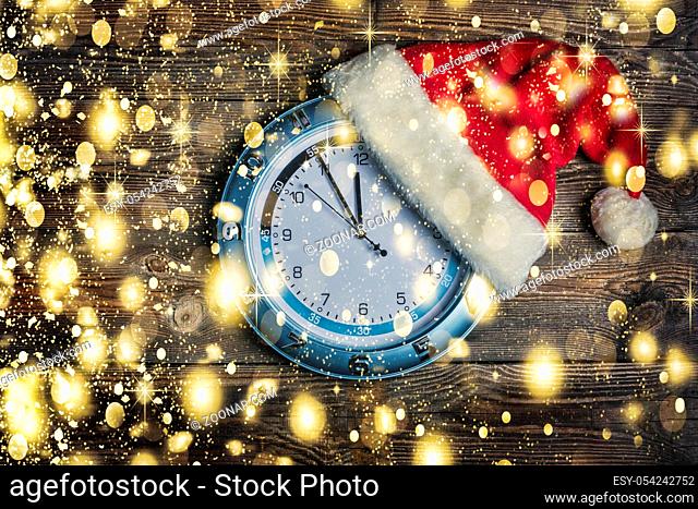 Concept: Christmas and New Year. Santa's hat is worn on wall clock and arrows show approaching New Year's midnight. on wooden background with copy space and...