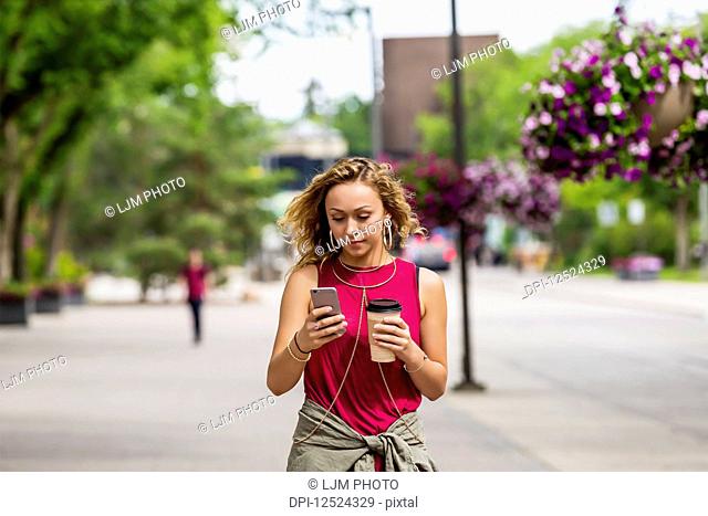 A young woman walking down a street near a university campus texting on her smart phone; Edmonton, Alberta, Canada
