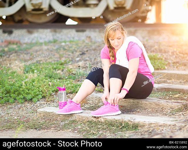 Young adult woman outdoors with towel and water bottle tying her shoe ready for workout