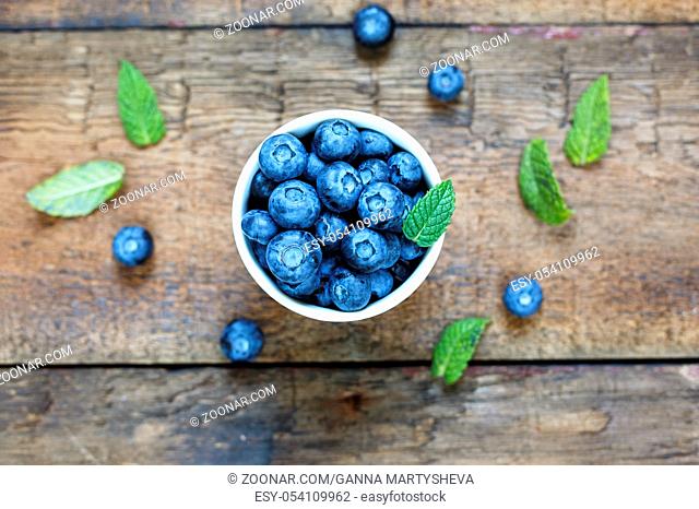 Blueberries in a white bowl and mint leaves on a wooden background, rural style, top view