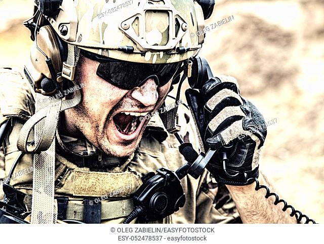 Special forces soldier, military communications operator or maintainer in helmet and glasses, screaming in radio during battle in desert