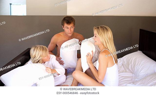 Parents and son having a pillow fight on bed