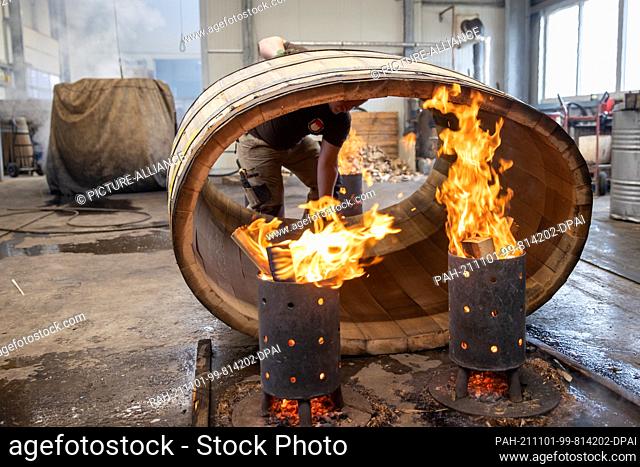 PRODUCTION - 11 October 2021, Bavaria, Eußenheim: The beader Tobias Schween from the beadery Aßmann places a barrel over fire bowls for firing