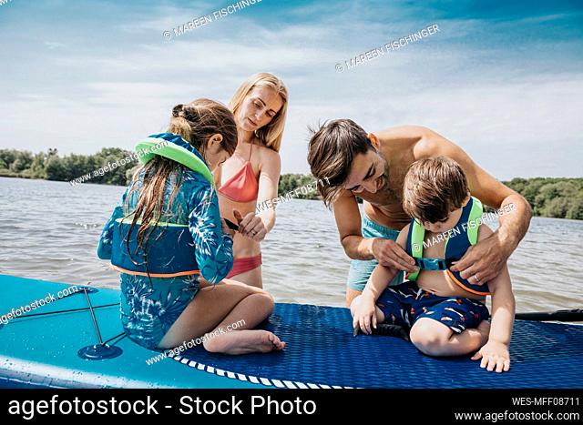 Parents fastening life jacket for their children in lake