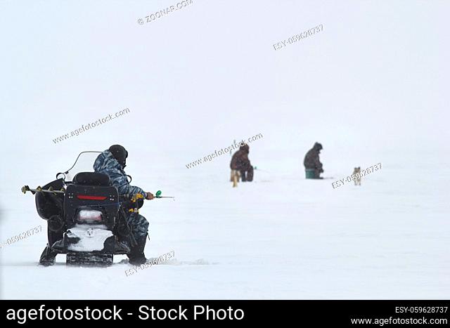 Ice fishermans - men on ice fishing caught fish at lake, telephoto shot