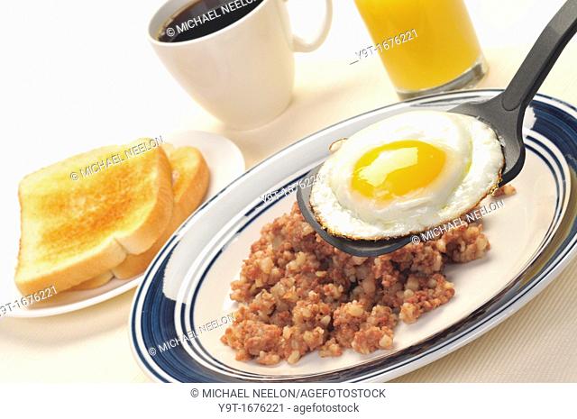 American blue plate breakfast special of a fried egg with cornbeef hash, toast, glass of orange juice and coffee closeup on white
