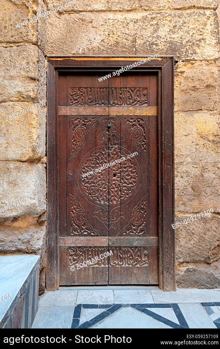 Wooden ornate door with geometrical engraved patterns on external old decorated bricks stone wall, Sultan Barquq mosque, Cairo, Egypt