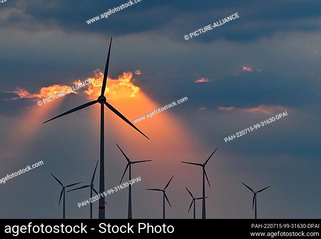 13 July 2022, Brandenburg, Mallnow: Colorful sunset shines through a gap in the clouds above wind turbines. Photo: Patrick Pleul/dpa