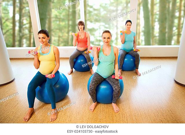 pregnancy, sport, fitness, people and healthy lifestyle concept - group of happy pregnant women with dumbbells exercising on ball in gym