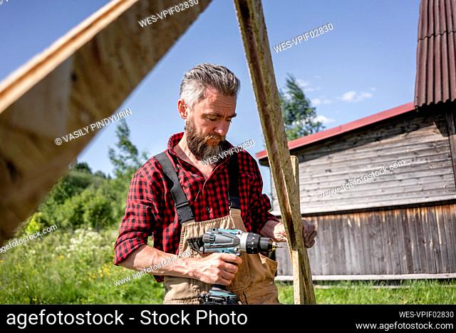 Carpenter man drilling with power tool while making playhouse