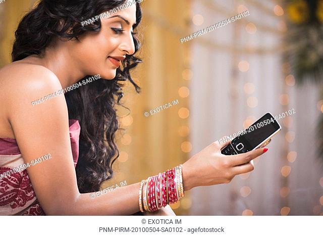 Bride in traditional Bengali dress text messaging on a mobile phone