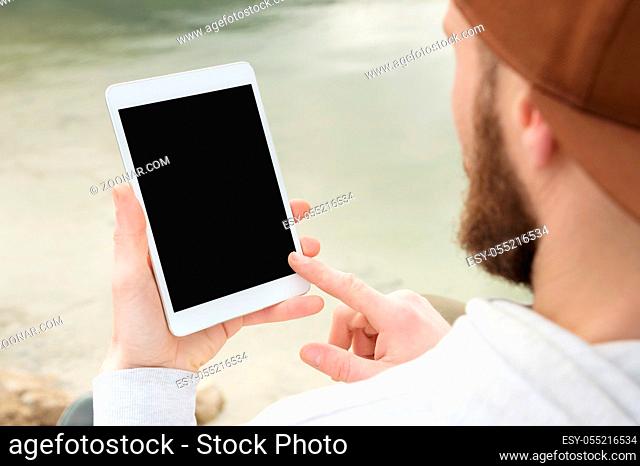 Close-up of a horde in a brown cap in the open air holds a white tablet pc in his hands. A bearded man looks at the tablet