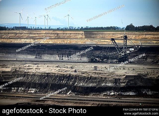 04 April 2022, North Rhine-Westphalia, Jackerath: Mining machines work in the Garzweiler open pit lignite mine, with wind turbines in the background