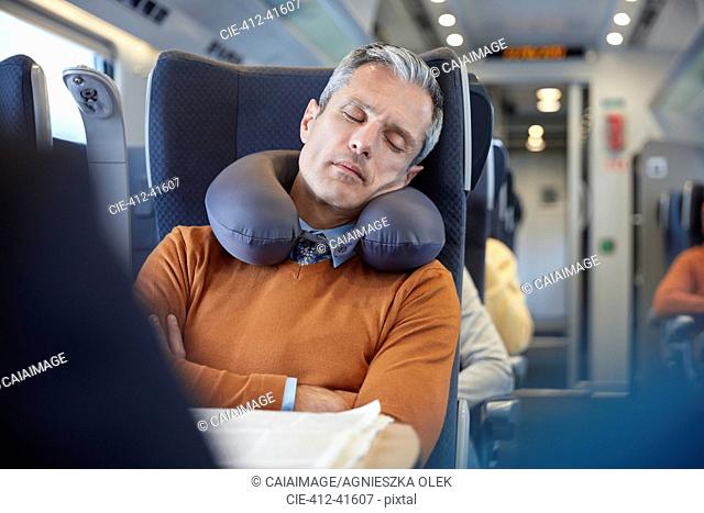 Tired businessman with neck pillow sleeping on passenger train